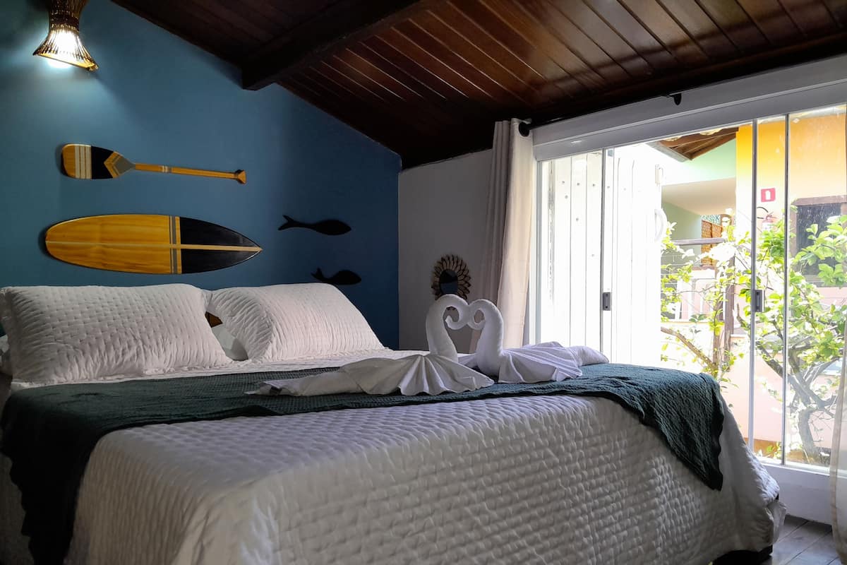 Ein Bett mit weißer Bettwäsche und einer grünen Decke, ein Holzschläger und zwei Bilder von Fischen an der Wand.