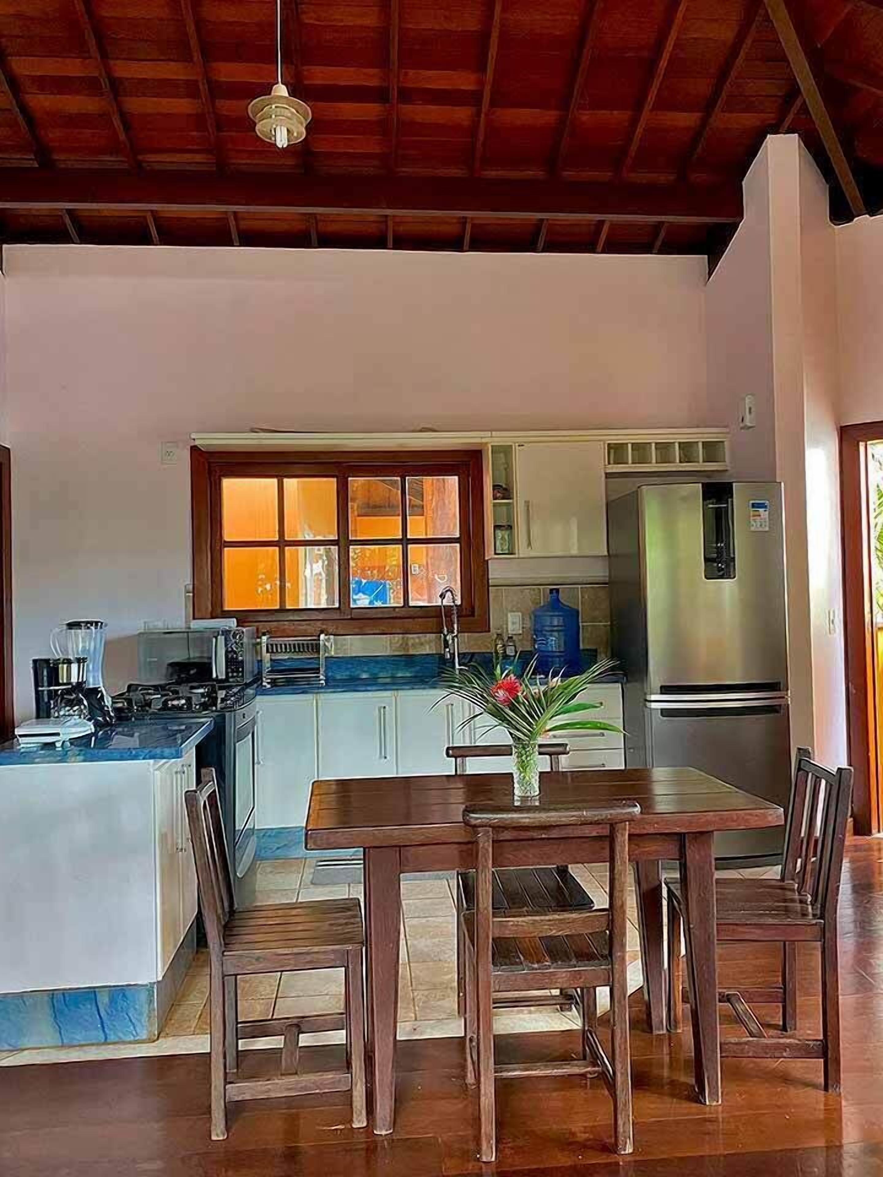 Uma cozinha com mesa e cadeiras de madeira, geladeira e janela com cortinas.
