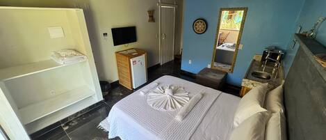 A hotel room with a bed, a TV, a small refrigerator, a wooden cabinet, a mirror, and a bathroom with a sink and toilet.