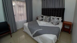 Ein modernes Hotelzimmer mit einem großen Bett, grauen Vorhängen, einem hölzernen Nachttisch und einem kleinen Tisch.