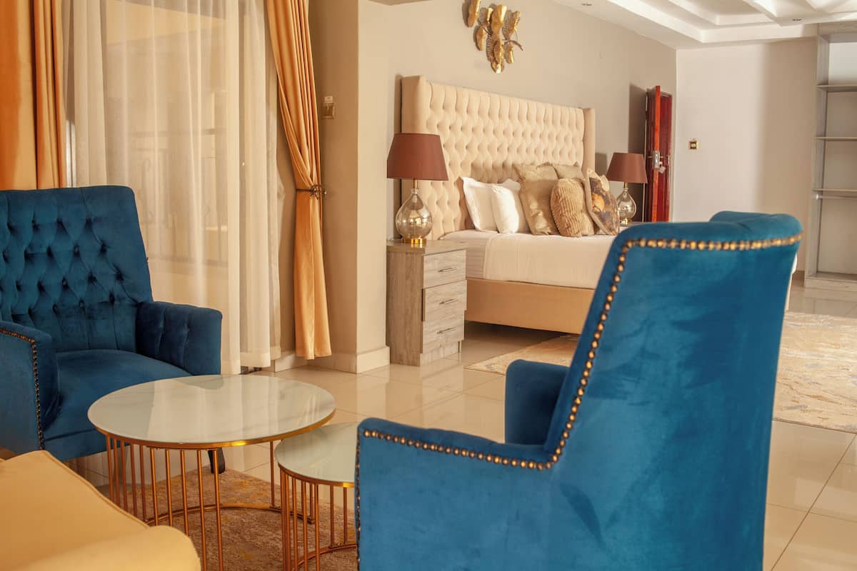 Una habitación de hotel moderna con una cama de cabecera capitonada, un sillón azul, una mesa de centro redonda de vidrio y un sofá beige.