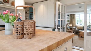 Una cocina con encimera de madera, cestas de mimbre y un florero con tulipanes rosados.