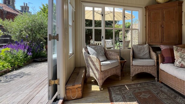 Una habitación iluminada por el sol con muebles de mimbre, un aparador de madera y vistas a un jardín.