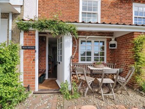 A brick cottage with a white door, a small table with chairs, and a sign reading "BETA COTTAGE". - Beta Cottage (Reydon)