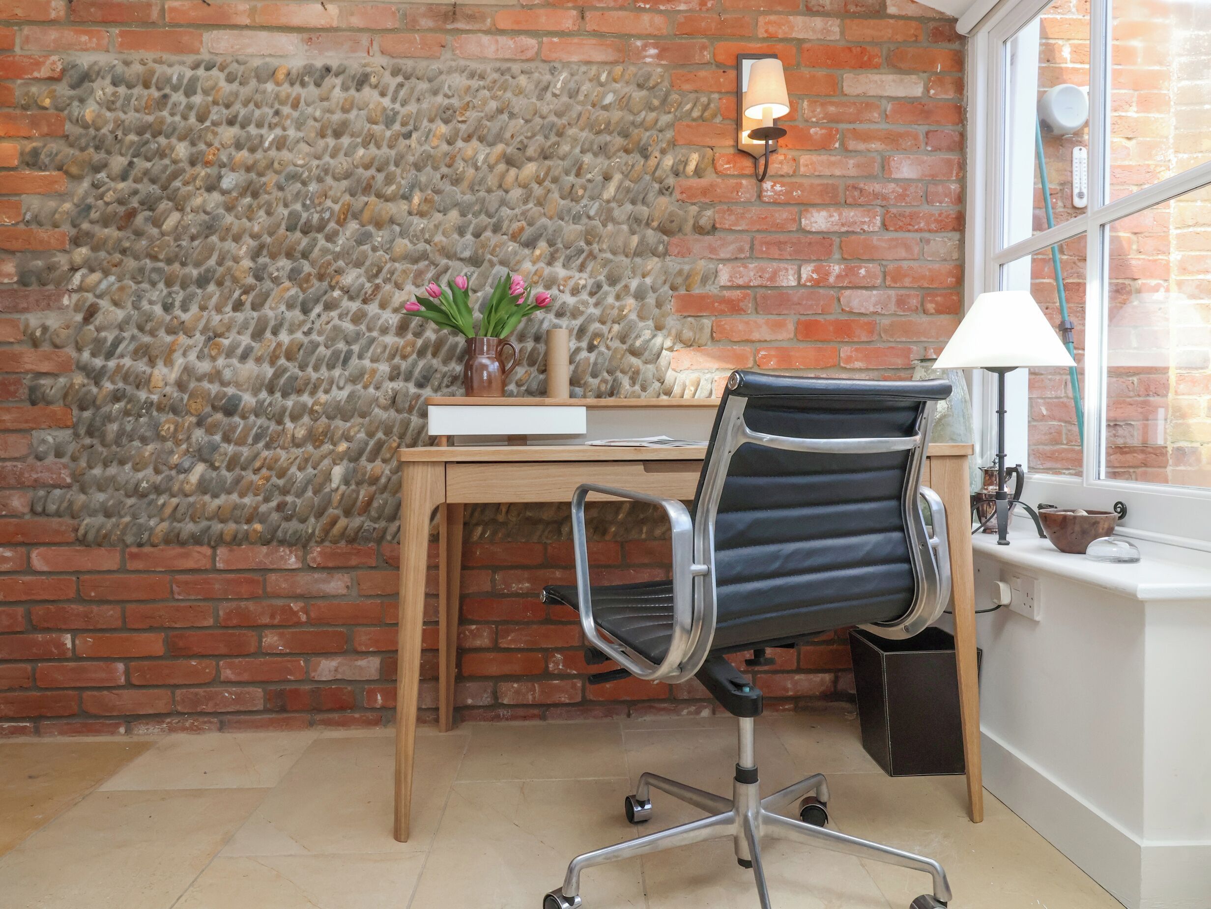 A workspace with a desk, chair, and a stone wall.