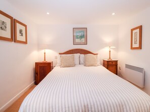 A neatly arranged bedroom with a large bed, two bedside tables, and a wall-mounted radiator. - Beta Cottage (Reydon)