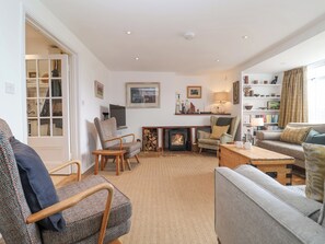 A cozy living room with a fireplace, comfortable seating, a bookshelf, and a dining area. - Beta Cottage (Reydon)