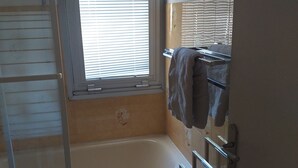 Un baño con bañera, una ventana con persianas, un perchero y una zona de ducha.