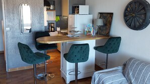 Cocina compacta con encimera de madera, dos taburetes de bar, un refrigerador y un reloj en la pared.