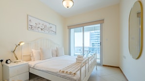A modern bedroom with a bed, bedside table, lamp, and a large window with a view of buildings.