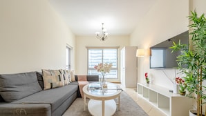 A modern living room with a grey sofa, a glass coffee table, a TV mounted on the wall, and a large potted plant.