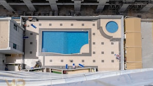 A large indoor swimming pool with a tiled deck surrounding it, a circular fountain, and a covered area with a roof.