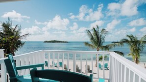 A wooden deck with green chairs overlooking a beach with clear blue water and a small island in the distance. - Guana Beach Inn (Great Guana Cay)