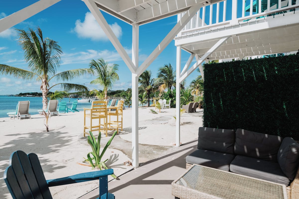 A beachside patio with a white pergola, lounge chairs, and a sofa.