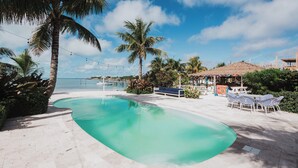 A swimming pool with a curved edge, surrounded by palm trees and a beach view. - Guana Beach Inn (Great Guana Cay)