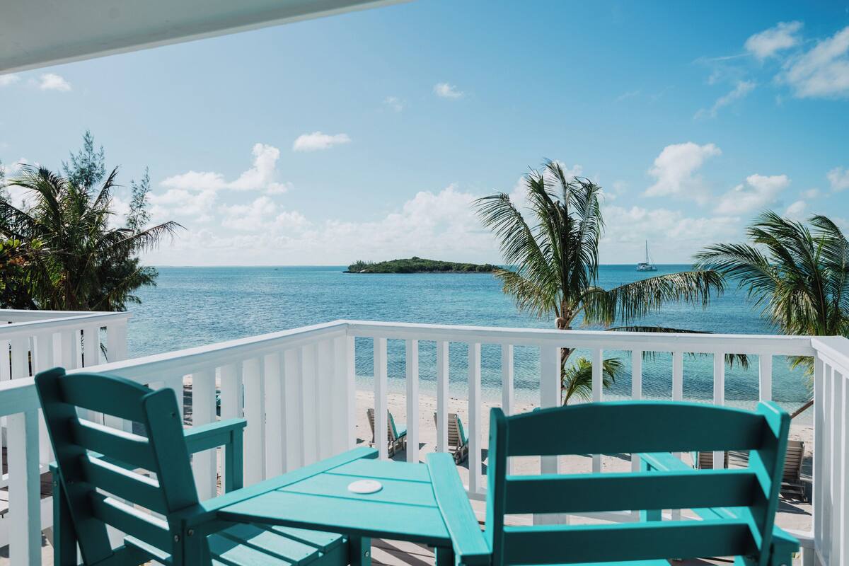A turquoise deck with white railings overlooking a beach and ocean.