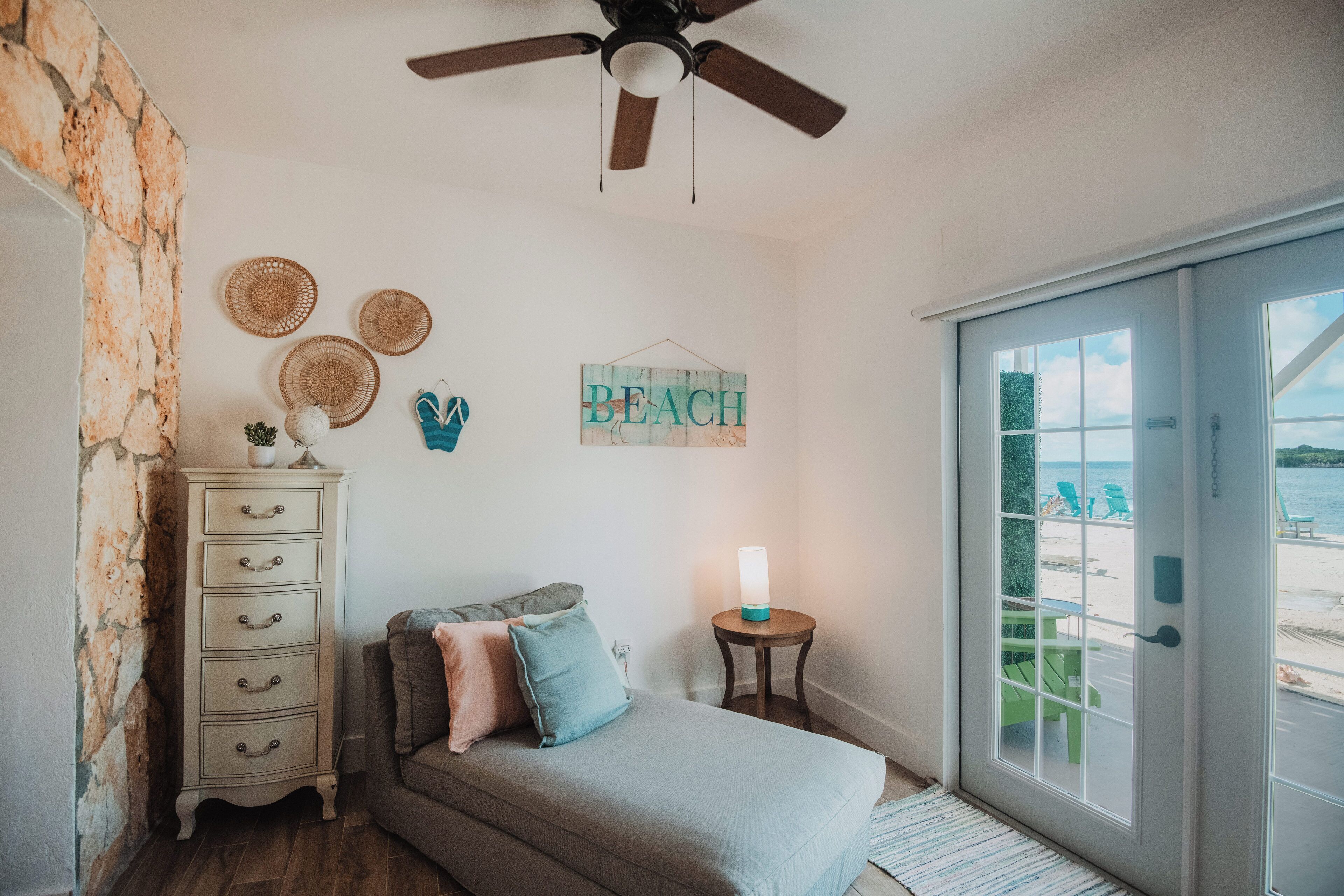A bedroom with a bed, dresser, wall decor, and a view of the beach through a sliding door.