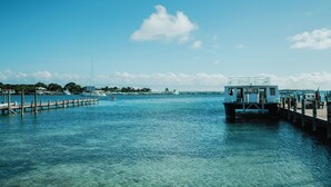 A waterfront dock with a small building, clear blue water, and a distant pier. - Guana Beach Inn (Great Guana Cay)