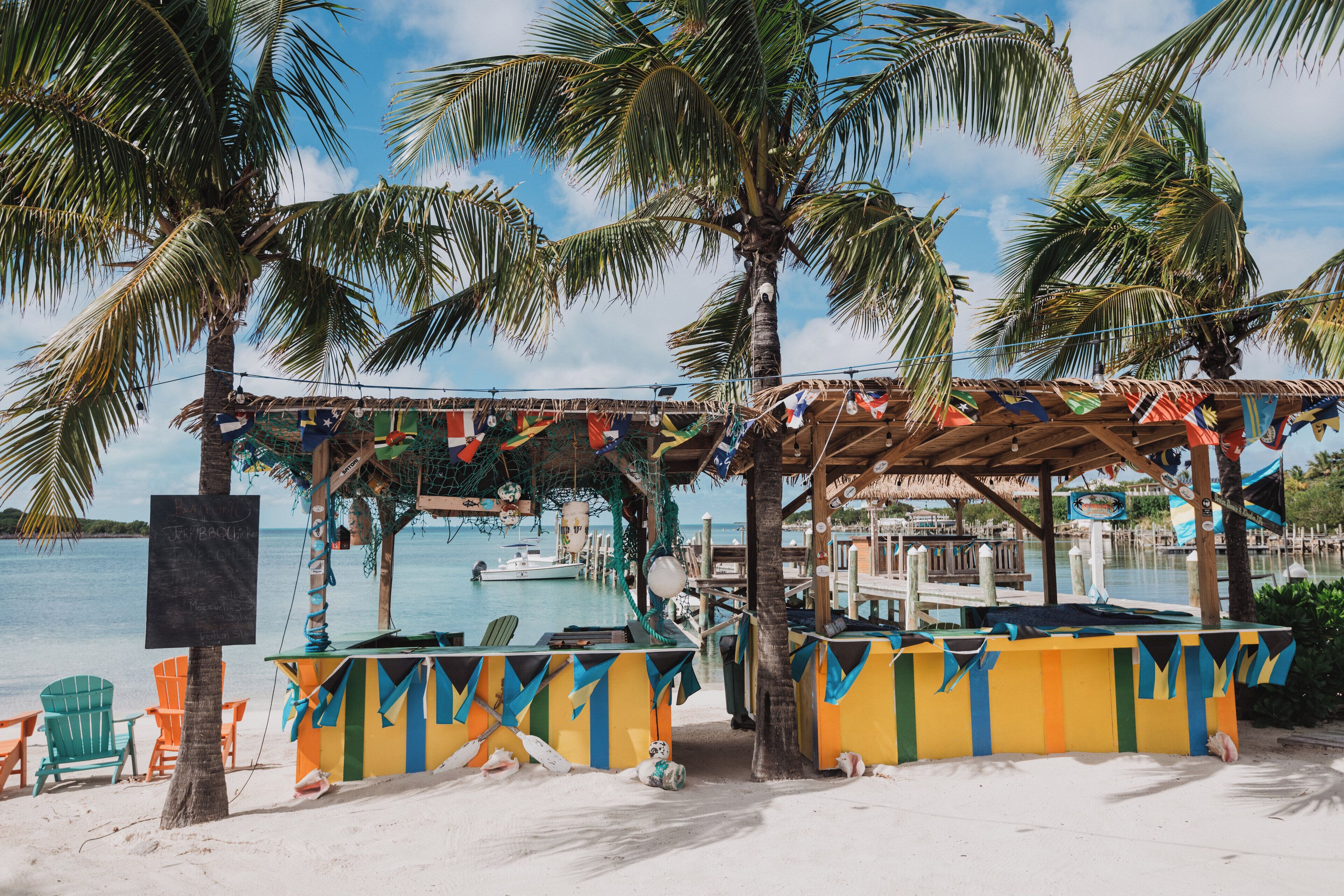A beachside bar with colorful decorations, palm trees, and a view of the sea.