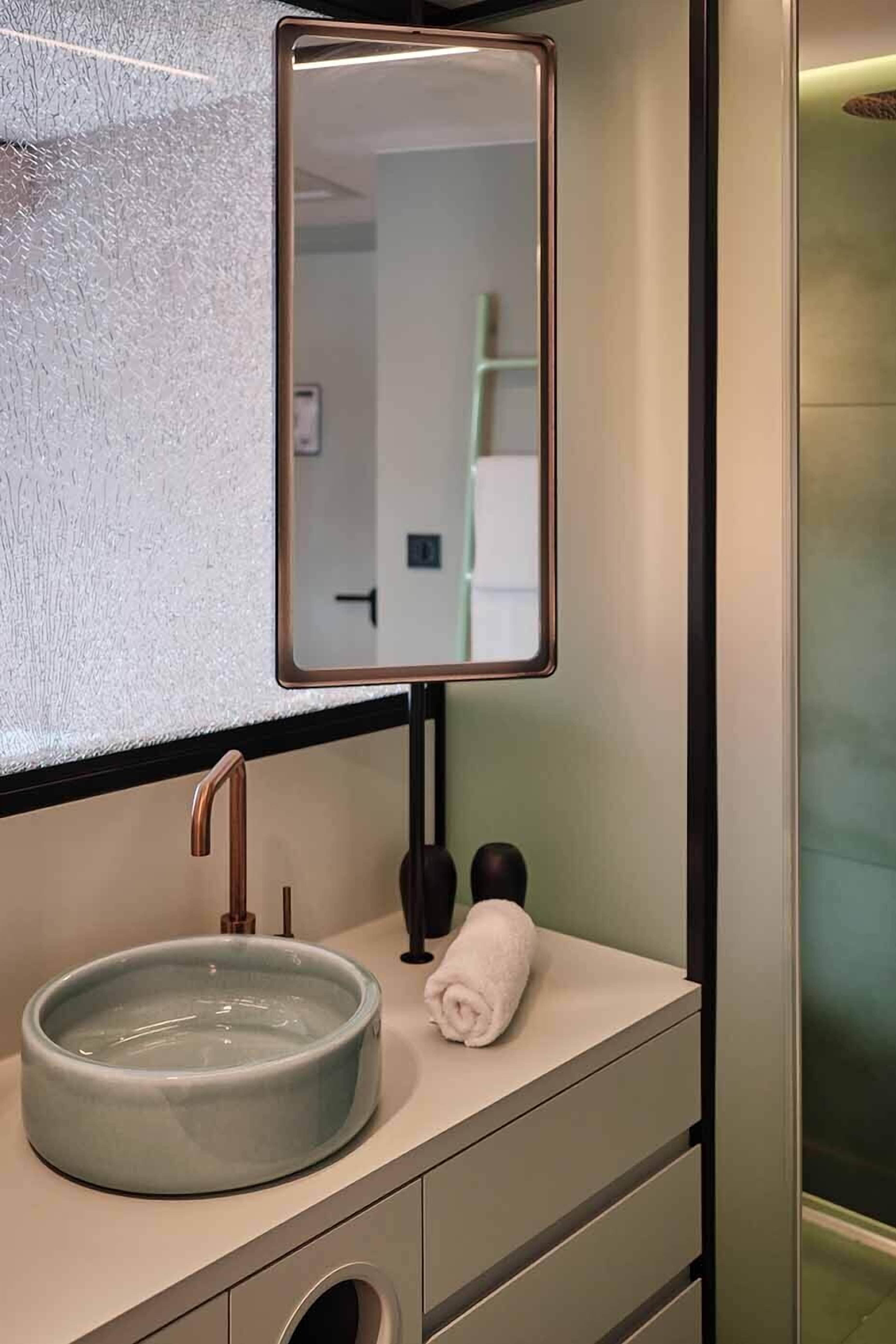 Un baño con un lavamanos redondo, un espejo y una toalla sobre el mostrador.