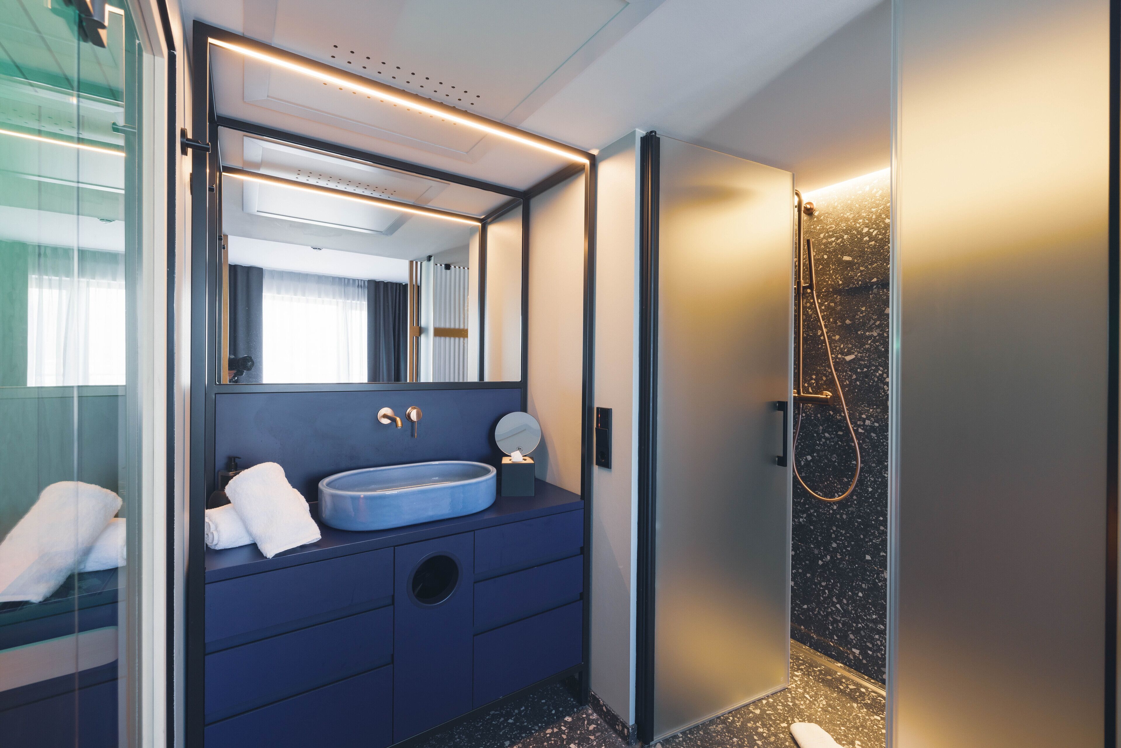 Un bagno moderno con un lavandino blu, uno specchio e una doccia.
