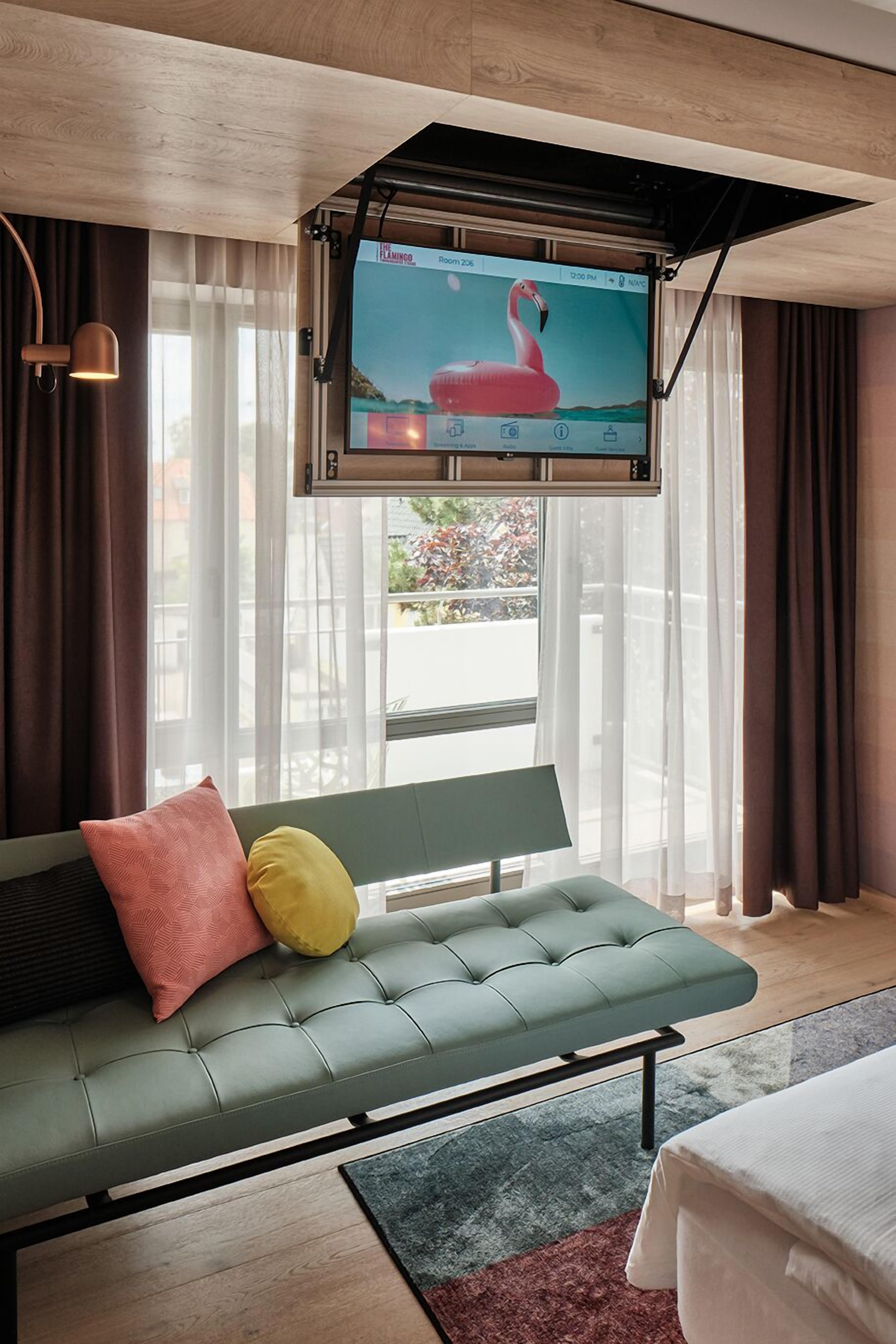 Habitación de hotel moderna con sofá verde, televisor de pantalla plana montado en la pared y vistas al exterior a través de amplias ventanas.