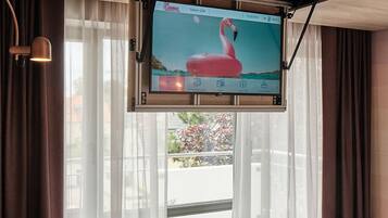 Habitación de hotel moderna con sofá verde, televisor de pantalla plana montado en la pared y vistas al exterior a través de amplias ventanas.