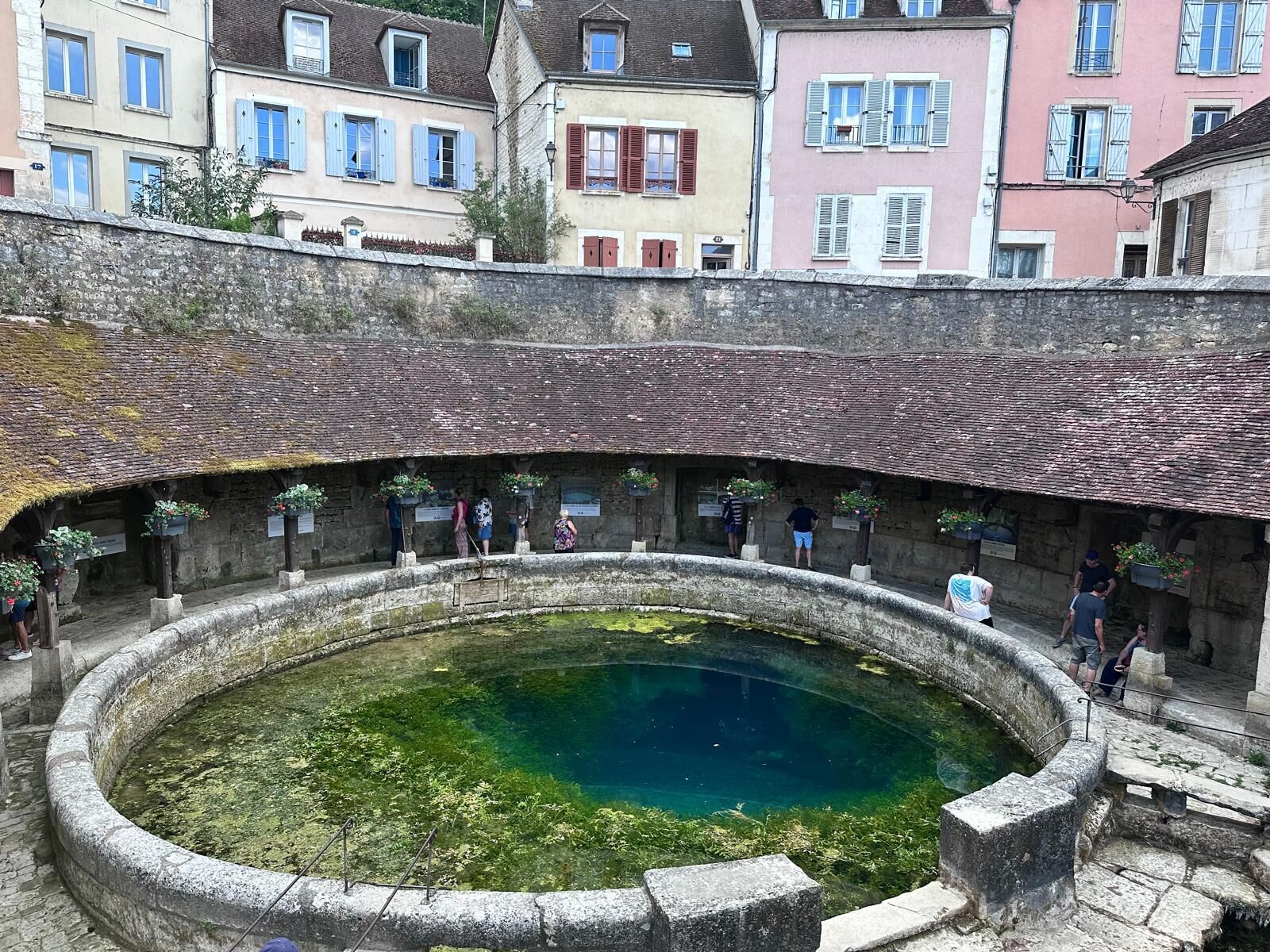 Un antico pozzo in pietra con superficie d'acqua cristallina, circondato da mura in pietra e un tetto in pietra.