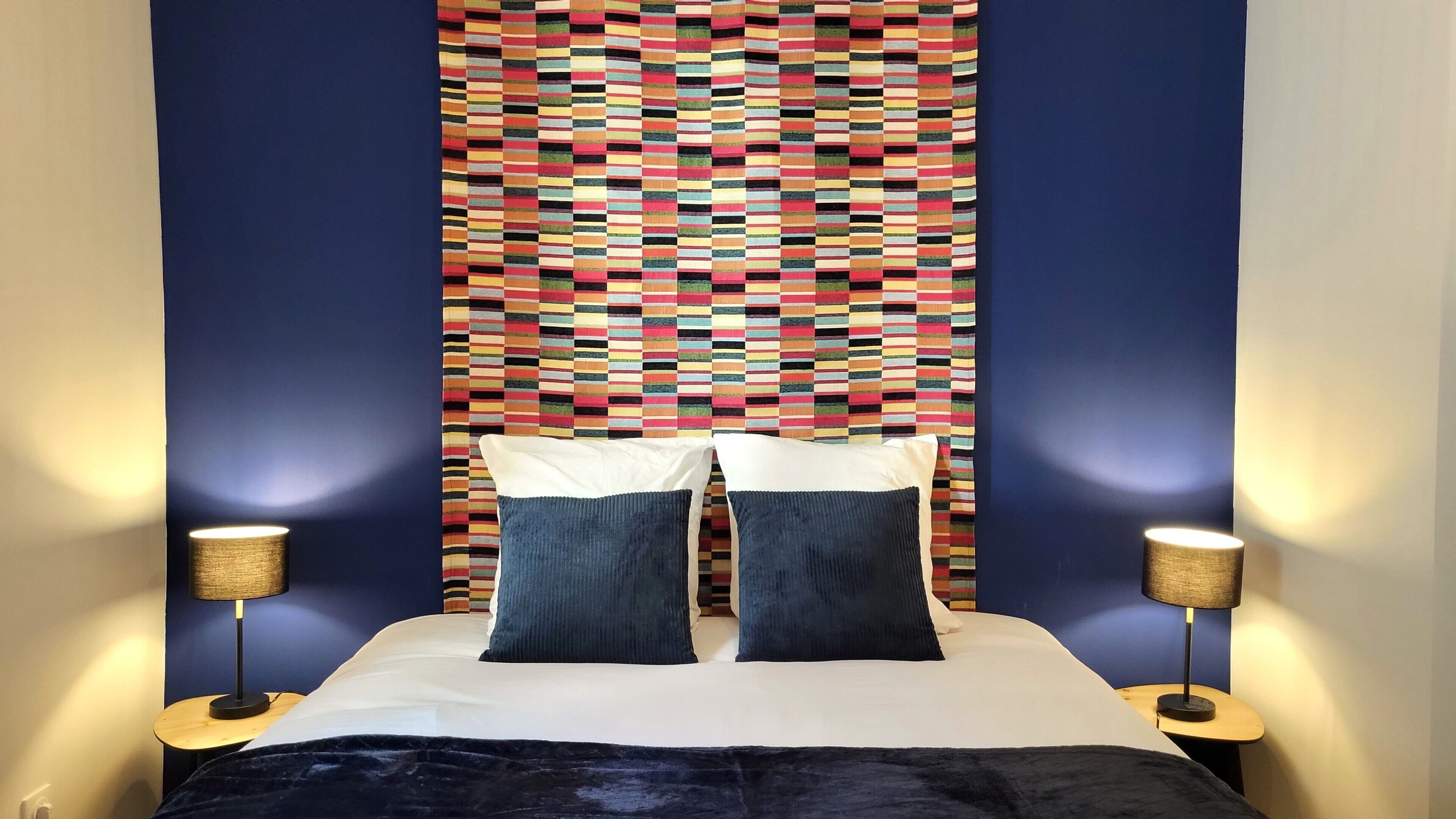 Een hotelkamer met een bed, twee bedlampjes en een kleurrijke gestreepte wand.