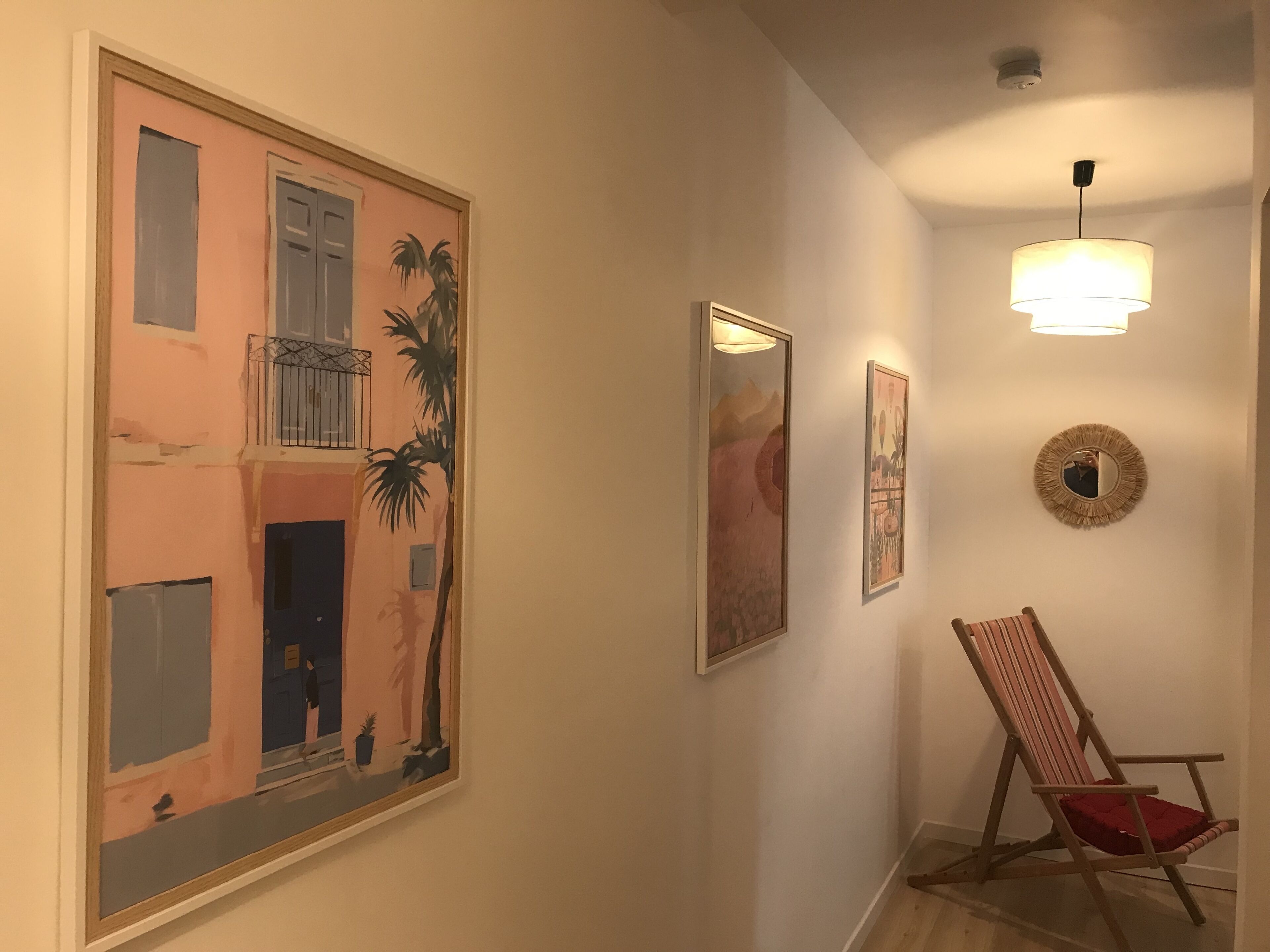 Un pasillo con un cuadro grande enmarcados de un edificio, una silla de madera y un espejo fijado a la pared.