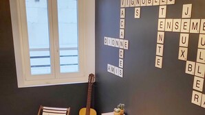 A room with a window, a guitar, a striped chair, a bookshelf, and a Scrabble game on the wall. - Home Antonin & Maye: 6 travelers - 3 bedrooms - 2 bathrooms - Terrace (TONNERRE)