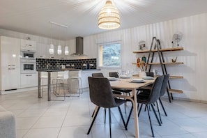 Une cuisine moderne avec des meubles blancs, un îlot central et un coin repas comprenant des chaises et une table.