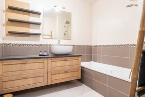 A bathroom with a wooden vanity, a large mirror, a white sink, and a bathtub.