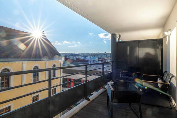 A balcony with a view of buildings, a table, and two chairs.