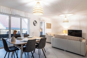 A modern living room with a dining area, a sofa, a TV, and a large window.