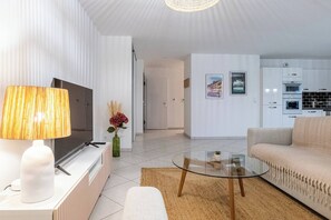 A modern living room with a TV, sofa, glass coffee table, and kitchen in the background.