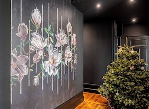 Une piÚce avec un grand décor mural floral, un sapin de Noël et un plancher en bois.