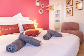 Ein Hotelzimmer mit einem Bett, Kissen, einem Sessel, einer Ablage mit Aufbewahrungsboxen und gerahmten Bildern an der Wand.