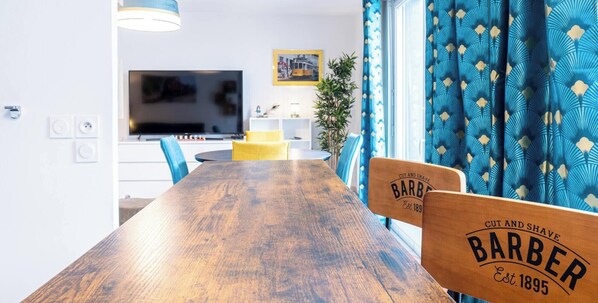 Et moderne spiseområde med et træbord, blå stole, et fjernsyn og en plante.