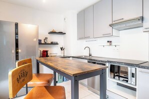 Et moderne køkken med et træbord, en barstol, stålstål-hvidelementer og hårde hvide hvidevarer.
