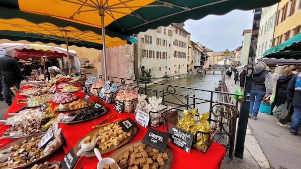 A street market with various food stalls, a canal, and buildings in the background.