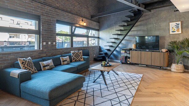 A modern living room with a brick wall, a staircase, a sofa, a coffee table, and a television.