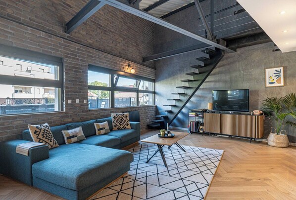 A modern living room with a brick wall, a staircase, a sofa, a coffee table, and a television.