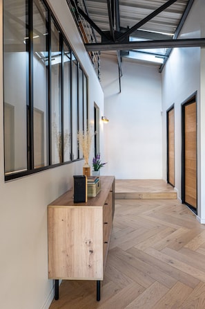 A hallway with a wooden floor, a wooden console table, a vase with dried plants, and a door with a wooden frame.