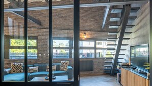 A modern interior with a brick wall, a sofa with patterned cushions, a wooden floor, and a bar area with a TV.