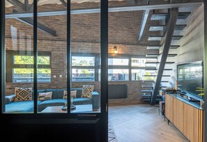 A modern interior with a brick wall, a sofa with patterned cushions, a wooden floor, and a bar area with a TV.