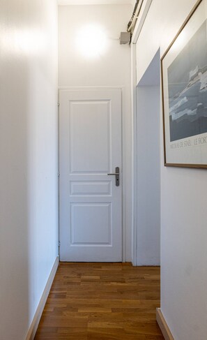 Un couloir avec une porte blanche, un plancher en bois et un tableau encadré accroché au mur.