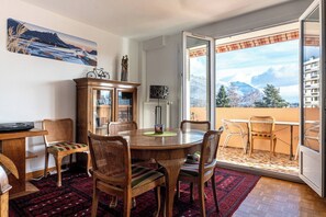 En spiseplads med et rundt bord og stole, et skab og udsigt til bjerge gennem en glasdør.