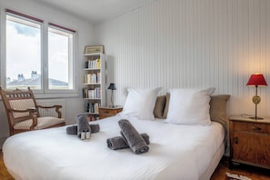 A neatly made bed with rolled towels, a bookshelf, a chair, and a nightstand with a lamp.