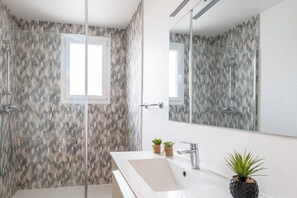 Uma casa de banho moderna com chuveiro, pia, espelho e duas plantas em vasos.